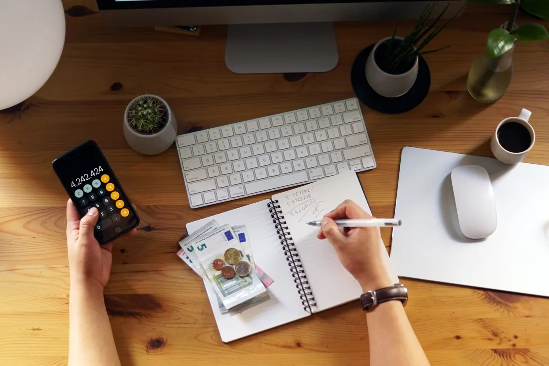 Kosten für die neue Website werden am Schreibtisch mit Taschenrechner und Notizbuch durchgerechnet